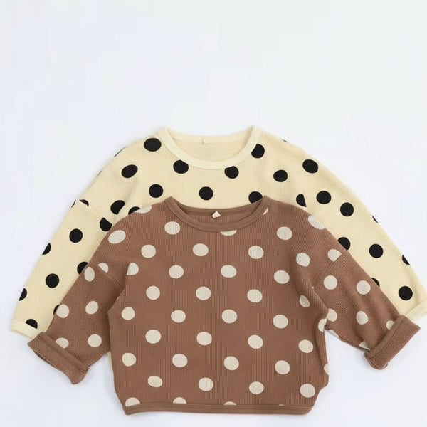 Two polka dot shirts, one beige with black dots and one brown with white dots, on a light blue background.