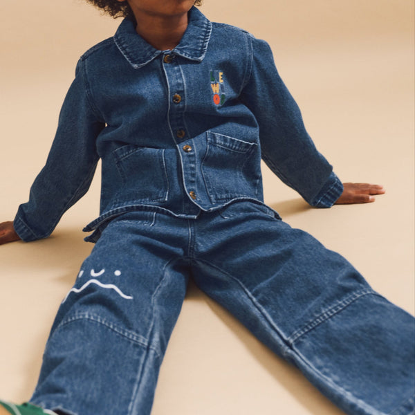 Child wearing a denim outfit sitting on a beige background