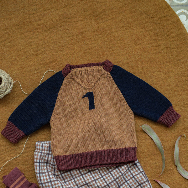 Knitted baby outfit with sweater, pants, and socks on a brown surface
