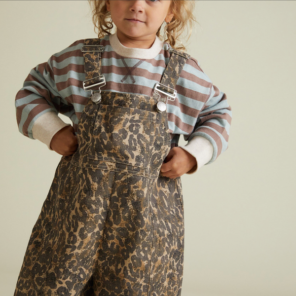 Child wearing a striped shirt and leopard print overalls on a plain background